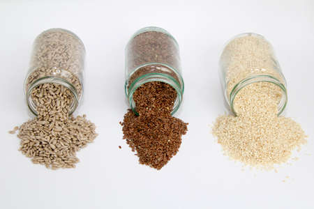 Glass jars with sunflower seeds, flax seeds and sesame, isolated on white backgroundの写真素材