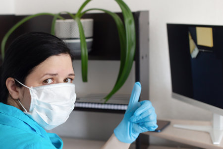 the woman at the computer wearing a protective mask and glovesの写真素材