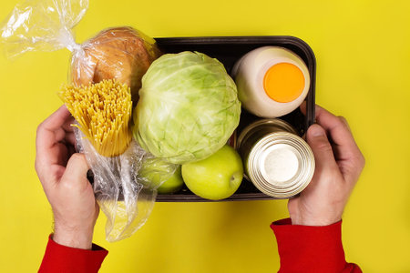 the box of groceries in hand on a yellow backgroundの写真素材