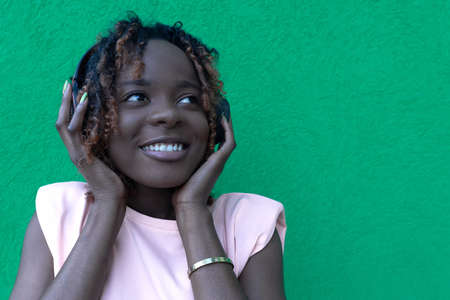 Young happy African-American woman in headphones on a green backgroundの写真素材