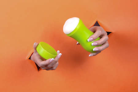 Adult sex toys in women's hands on an orange background.
