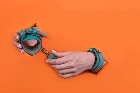 Adult sex toys, minimal design, isolated on an orange background. Women's hands in handcuffs.の写真素材