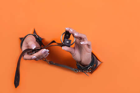 Adult sex toys, minimal design, isolated on an orange background. Women's hands in handcuffs. Bdsm.の写真素材