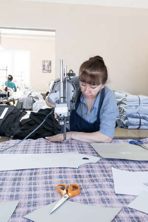 Textile industry, clothing production. A woman cuts cloth with an electric cutter.