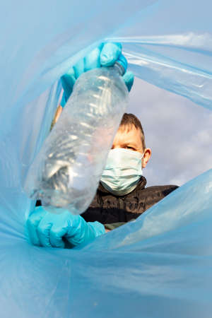 A volunteer wearing a protective mask throws an empty bottle into a garbage bag.