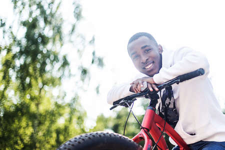 A young African-American man in nature with a bicycle.