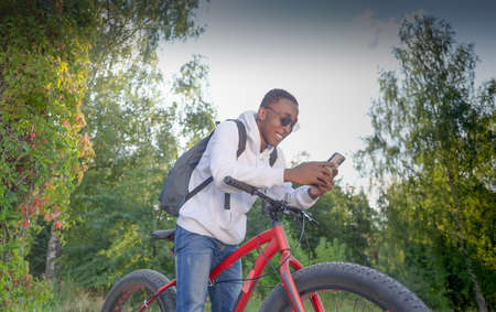 An African-American man with a phone in his hands and a bicycle.