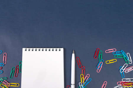 A notebook with a pen and paper clips on a blue background. School and office supplies.の写真素材