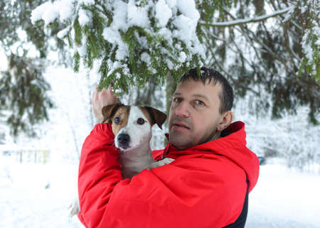 A smiling man holds a purebred dog in his arms. Jack Russell Terrier. Pets in winter.