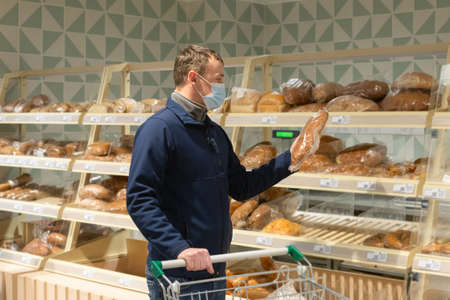 A man in a protective face mask chooses bread. Quarantine. lifestyle. food and drinks.の写真素材
