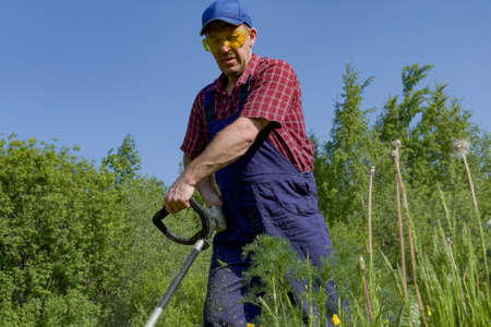 A man in protective glasses mows the grass with a lawn mower. A working farmer. cutting grass.