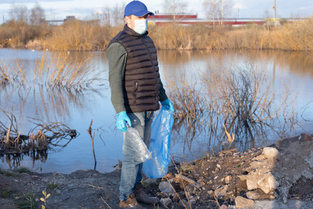 A volunteer in a protective face mask collects garbage. Ecology and the environment.の写真素材