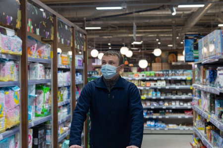 A man in a protective face mask chooses goods in a supermarket. retail trade. Quarantine.の写真素材