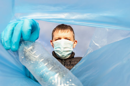 A man in a protective mask throws an empty bottle into a garbage bag. Ecology.の写真素材