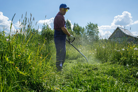 A man mows the grass with a gasoline trimmer in the open air. Gardening.