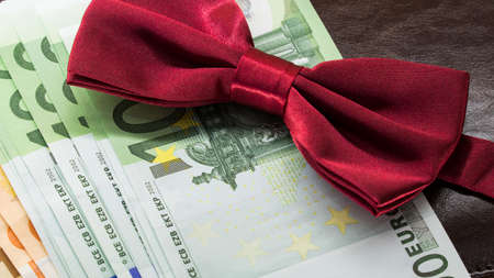 money in an envelope on a brown notepad background and red bow tieの写真素材