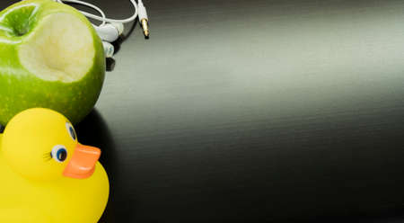 white headphones, a yellow duck and a green apple on a black computer