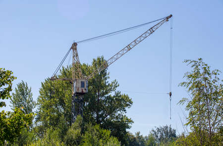 Old abandoned rusty tower crane on the background of trees and blue sky.の写真素材