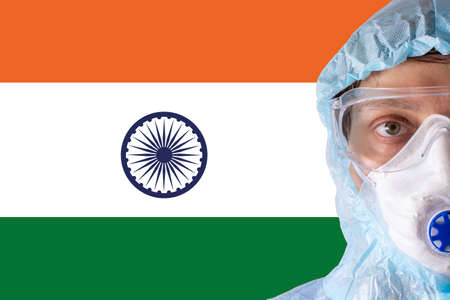 Man close-up in white protective suit, mask, glasses and gloves on the background of the flag of India, coronavirus pandemic threat. Epidemic, pandemic of coronavirus covid-19. Doctor in respirator.の写真素材