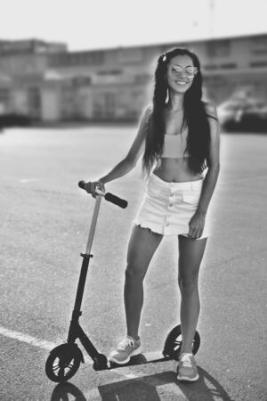 Girl with a scooter in the parking lot near the shopping center, summer, back light, smile and a good mood, the evening sun black and white photographyの写真素材