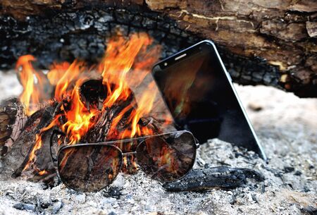 Sunglasses and telephone are burning in the bright flame of the fire, ash firewood close-upの写真素材