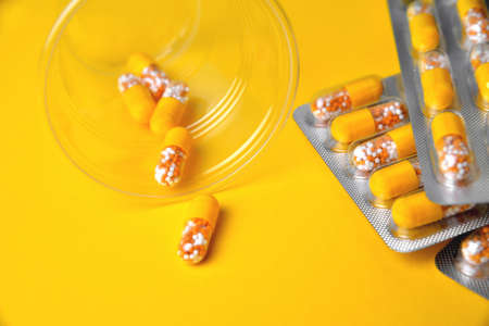 Capsules in a blister and a glass. Medical tablets, vitamins in a granule, in yellow capsules on a...