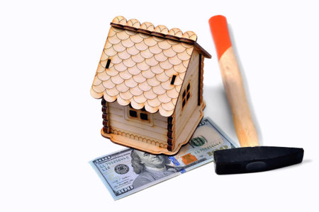 Wooden toy house, a banknote of 100 dollars and a hammer on a white background, isolate