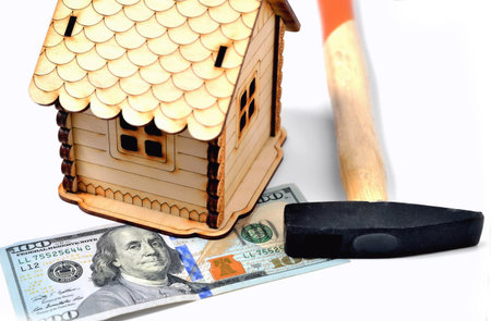 Wooden toy house, a banknote of 100 dollars and a hammer on a white background, isolate