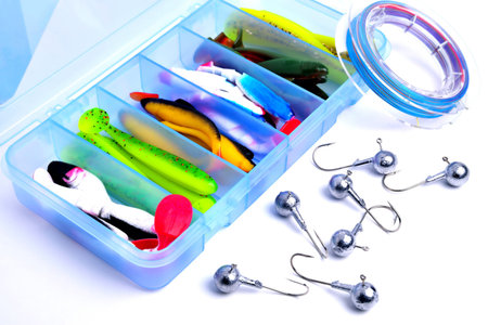 Box for fishing accessories with silicone baits inside, Jig hooks, braided reel on a white...