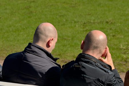 Warm summer day two men sit on a bench and bask in the sun.の写真素材