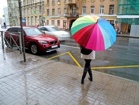 Girl hiding from the rain under an umbrella.She's waiting at the bus stop.の写真素材