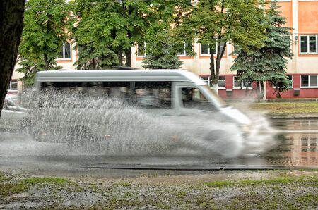 Cars move on asphalt through a huge puddle.Splashes from puddles razletayutsya in different directions.の写真素材