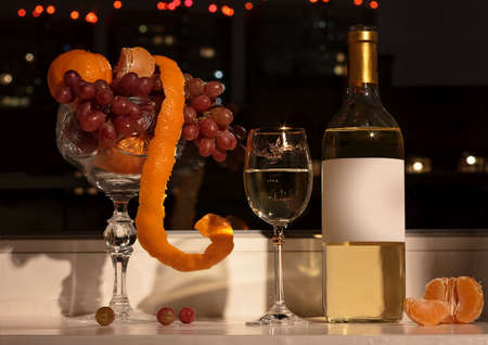 Fruit still life with grapes, wine and wine glass with wine, tangerines on a background of of the night city.の写真素材