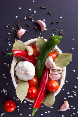Spices are scattered around the basket with pepper, garlic and tomatoes with bay leaf.の写真素材