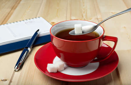 Cup of with tea on saucer, with sugar and spoon on a wooden background.の写真素材