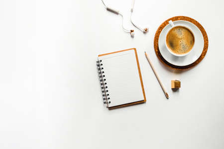 White desktop with cup of coffee and notebook and headphones.
