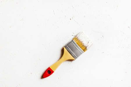 Covered in white paint construction brush. White painted plywood background. Flat lay, top view.の写真素材