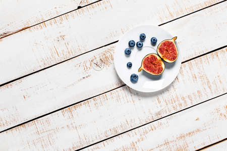 Autumn, fall concept. Figs and blueberries on a plate on a white wooden background. Space for your text. Flat lay, top view.の写真素材