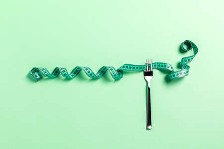 Sports and diet picture. Green measuring tape wound around the fork. Mint background. Flat lay, top view.の写真素材