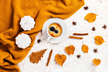 Autumn mood. Coffee surrounded by autumn leaves, cinnamon, pumpkins on a white and orange background of knitted sweaters.の写真素材