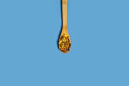 Dieting concept. Isolated blue background with fish oil capsules on the wooden spoon in the center of a picture. Flat lay, top view.の写真素材