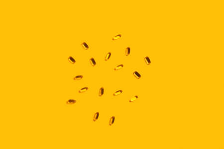Fish oil capsules on isolated yellow background.の写真素材