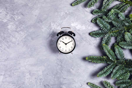 Christmas and new year composition. Black vintage clock with alarm on gray concrete background with Christmas branches. Flat lay, top view, copy space.の写真素材