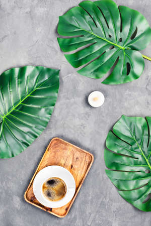 Grey concrete background with wooden tray and cup of espresso surrounded by tropical leaves. Flat lay, top view. Spa concept.の写真素材