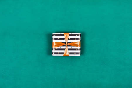 Present gift box tied with orange ribbon on green background. Flat lay, top view, copy space.の写真素材