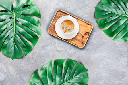 Gray concrete background with wooden tray and cup of espresso surrounded by tropical leaves. Flat lay, top view. Spa concept.の写真素材