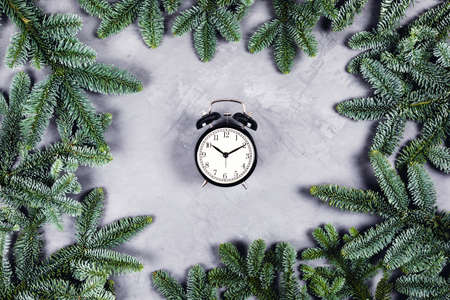 Christmas and new year composition. Black vintage clock with alarm on gray concrete background surrounded by Christmas branches. Flat lay, top view.の写真素材