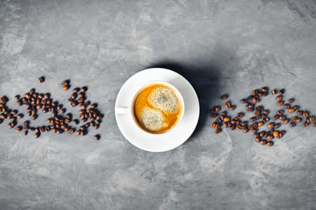 Gray concrete background with white cup of tasty coffee surrounded by coffee beans. Flat lay, top view, copy space.の写真素材