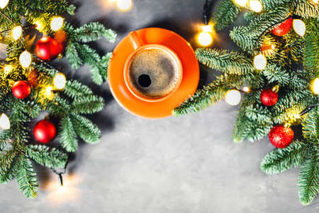 Christmas and New year composition with orange cup of coffee surrounded by fir brunches with red balls and on gray table.の写真素材