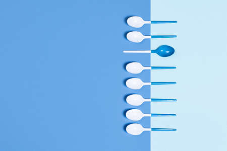 Beautiful and dangerous plastic spoons on two-toned blue background. Flat lay, top view, copy space.